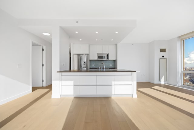 kitchen with a sink, stainless steel appliances, white cabinetry, dark countertops, and tasteful backsplash