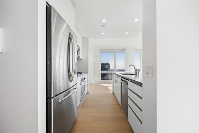 kitchen with light wood-style flooring, a sink, appliances with stainless steel finishes, white cabinetry, and modern cabinets