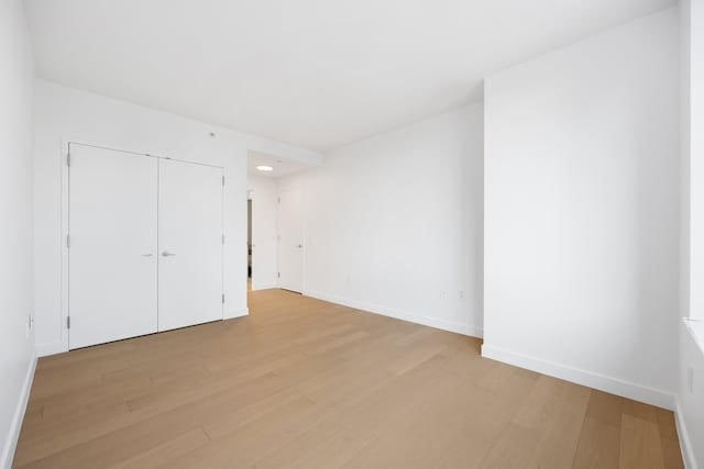 unfurnished bedroom featuring light wood-type flooring, baseboards, and a closet