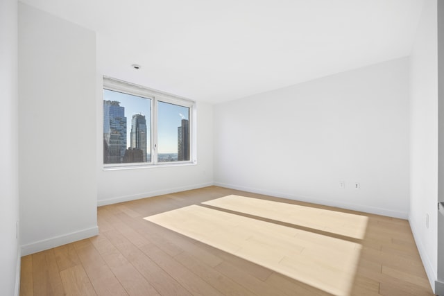 unfurnished room featuring a city view, light wood-style flooring, and baseboards