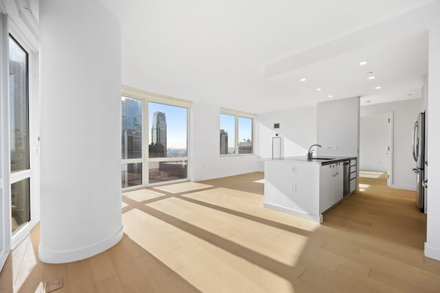 kitchen with baseboards, an island with sink, recessed lighting, light wood-style flooring, and a sink