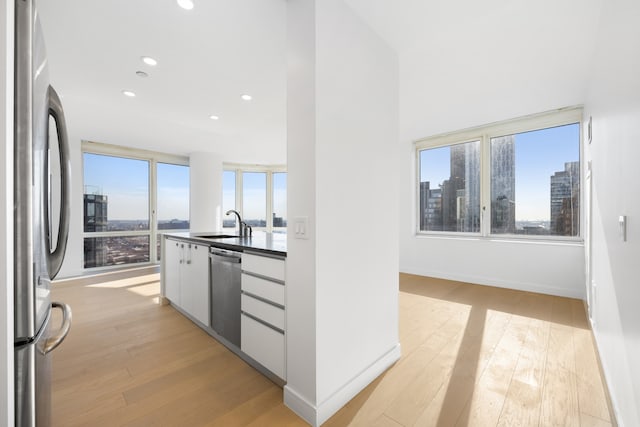 kitchen with light wood-type flooring, stainless steel appliances, dark countertops, and a wealth of natural light