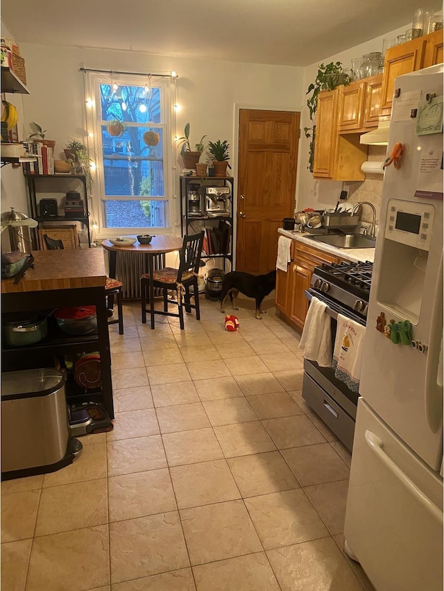 kitchen with light countertops, freestanding refrigerator, gas stove, light tile patterned flooring, and a sink