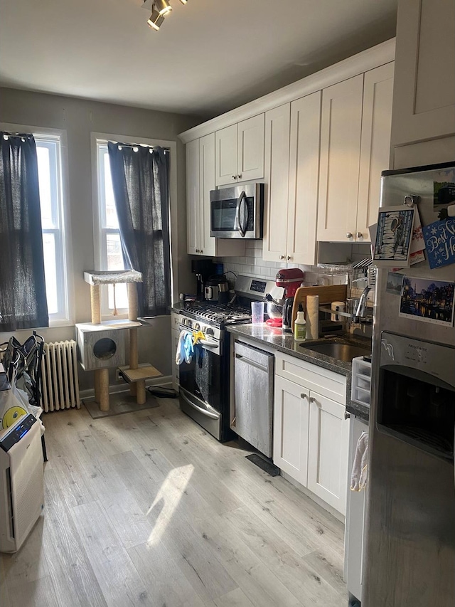 kitchen featuring stainless steel appliances, radiator, light wood-style flooring, backsplash, and white cabinets