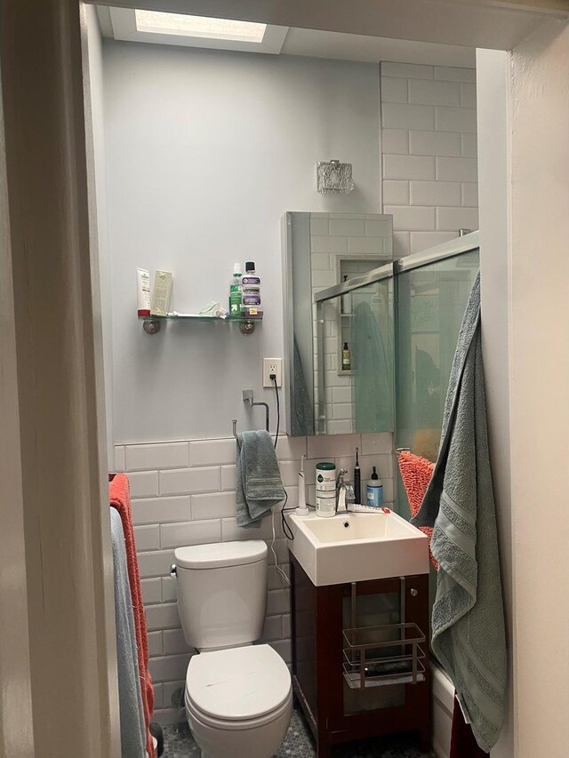 bathroom with toilet, a wainscoted wall, vanity, tile walls, and a shower stall