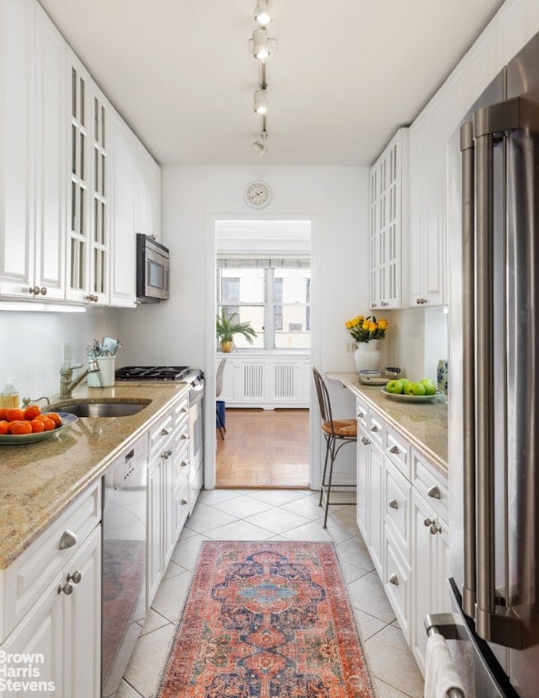 kitchen featuring light tile patterned flooring, sink, white cabinetry, light stone counters, and stainless steel appliances