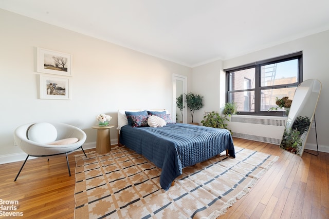 bedroom with baseboards, radiator, and hardwood / wood-style flooring