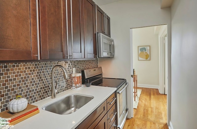 kitchen with sink, light hardwood / wood-style flooring, appliances with stainless steel finishes, tasteful backsplash, and dark brown cabinetry