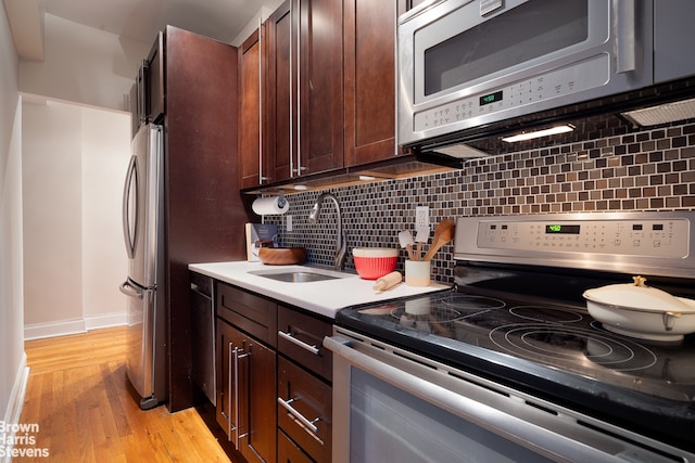 kitchen with backsplash, light countertops, appliances with stainless steel finishes, light wood-style floors, and a sink