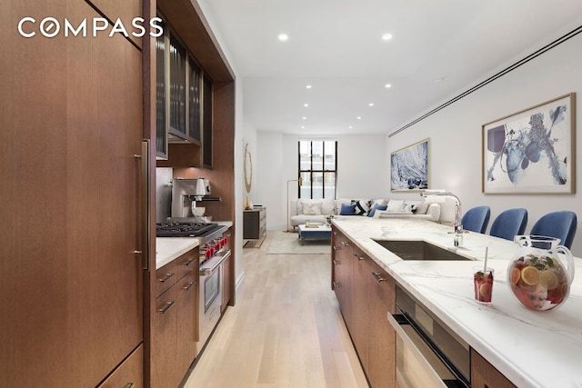 kitchen with a breakfast bar, sink, high end stainless steel range oven, light stone countertops, and light hardwood / wood-style floors