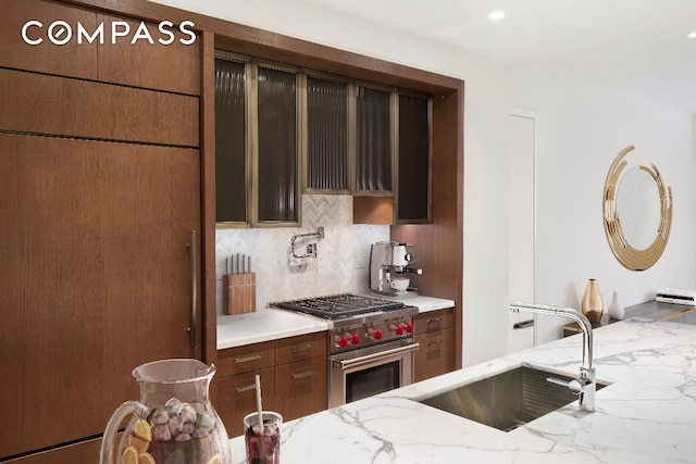 kitchen featuring light stone counters, high end stainless steel range, sink, and decorative backsplash