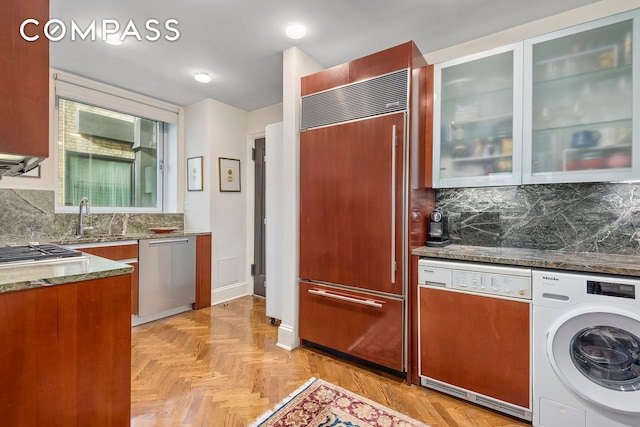 kitchen featuring tasteful backsplash, washer / clothes dryer, appliances with stainless steel finishes, a sink, and dark stone counters