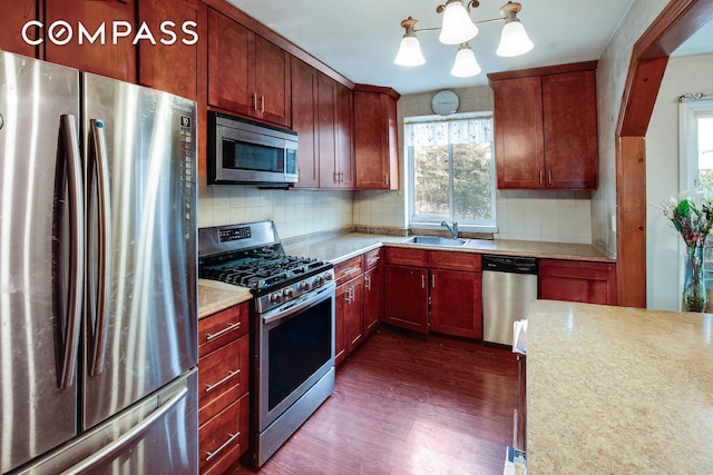 kitchen with a chandelier, decorative backsplash, dark wood-style floors, stainless steel appliances, and a sink