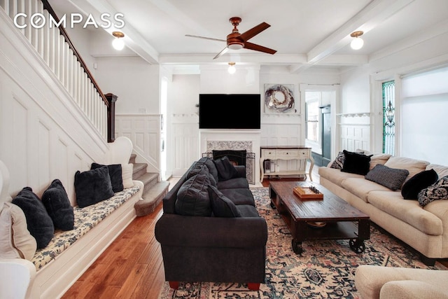 living room featuring hardwood / wood-style flooring, ceiling fan, beam ceiling, and a tile fireplace