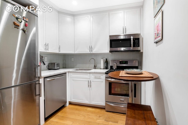 kitchen featuring appliances with stainless steel finishes, a sink, decorative backsplash, and light wood finished floors