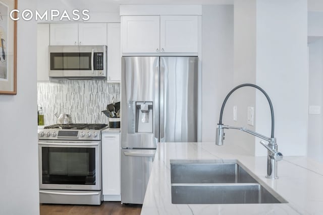 kitchen with white cabinets, light stone counters, stainless steel appliances, and a sink