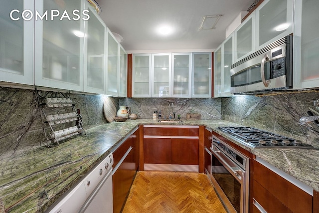 kitchen with stainless steel appliances, sink, light stone counters, light parquet flooring, and decorative backsplash