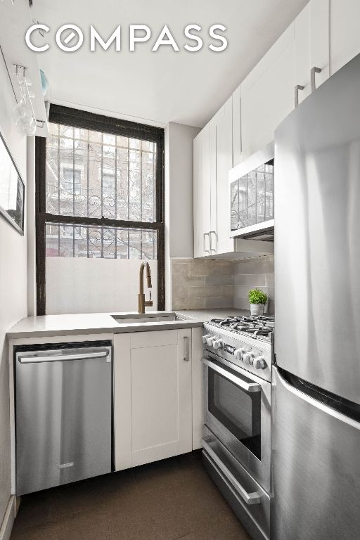 kitchen with tasteful backsplash, appliances with stainless steel finishes, sink, and white cabinets