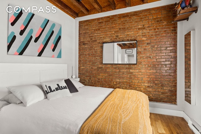 bedroom with brick wall, baseboards, baseboard heating, and wood finished floors