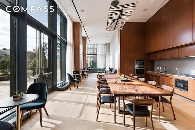 dining area with a wall of windows, light wood-style floors, and a towering ceiling