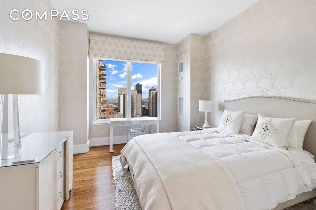 bedroom with a city view, light wood finished floors, visible vents, baseboards, and wallpapered walls