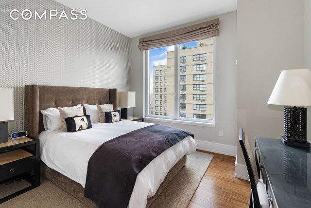 bedroom featuring an accent wall, wood finished floors, baseboards, and wallpapered walls