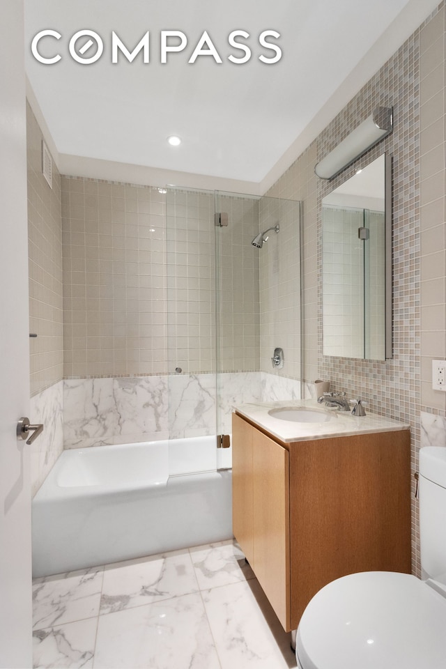 full bathroom with toilet, marble finish floor, tile walls, and a sink