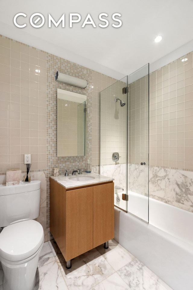 full bath featuring toilet, vanity, tile walls, marble finish floor, and combined bath / shower with glass door