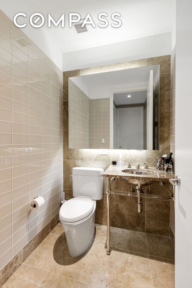 half bathroom with toilet, a sink, tile walls, and tile patterned floors