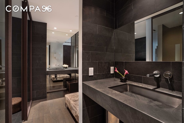 bathroom featuring tasteful backsplash, recessed lighting, wood finished floors, tile walls, and a sink