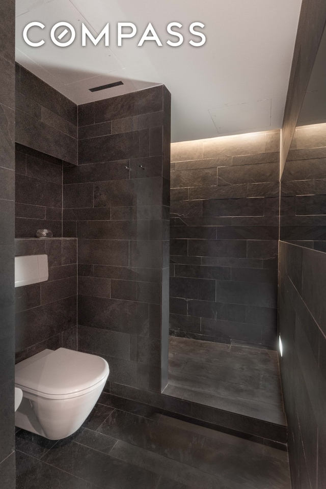 bathroom featuring a tile shower, toilet, and tile walls