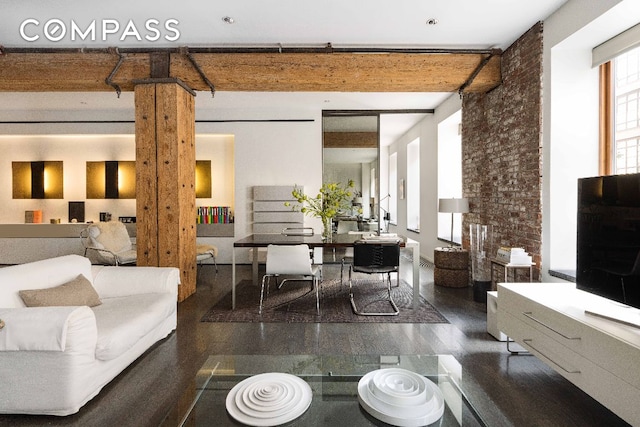 living room featuring dark wood-type flooring, ornate columns, and brick wall