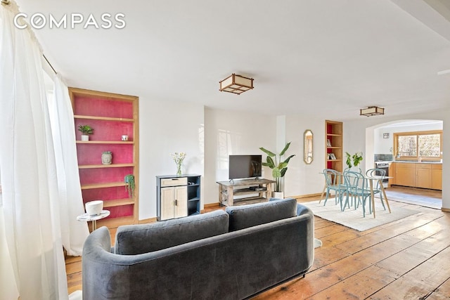 living room featuring built in features, arched walkways, baseboards, and wood finished floors