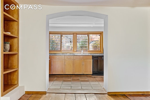 bar featuring light wood finished floors, baseboards, black dishwasher, arched walkways, and a sink