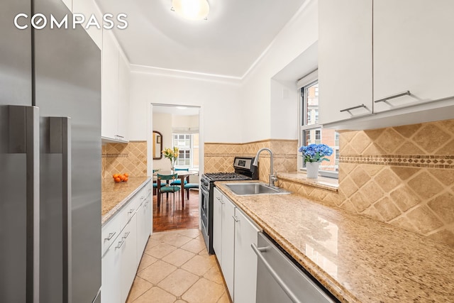 kitchen featuring light tile patterned floors, decorative backsplash, stainless steel appliances, white cabinetry, and a sink