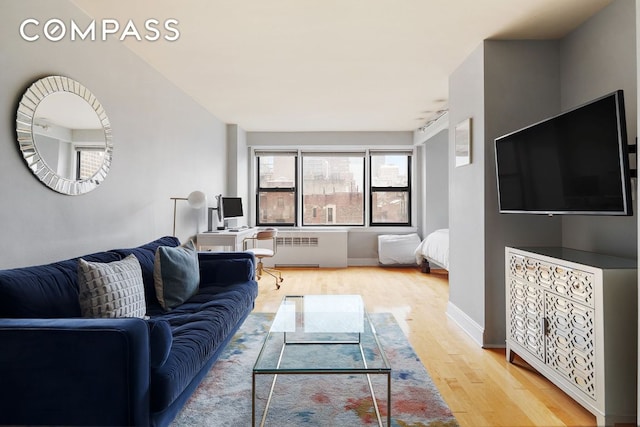 living area featuring baseboards, light wood-style floors, and radiator