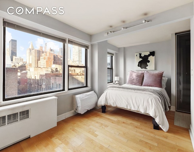 bedroom with light wood-type flooring, radiator heating unit, a view of city, and baseboards