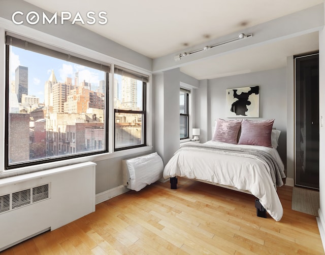 bedroom featuring a city view, radiator, baseboards, and hardwood / wood-style floors