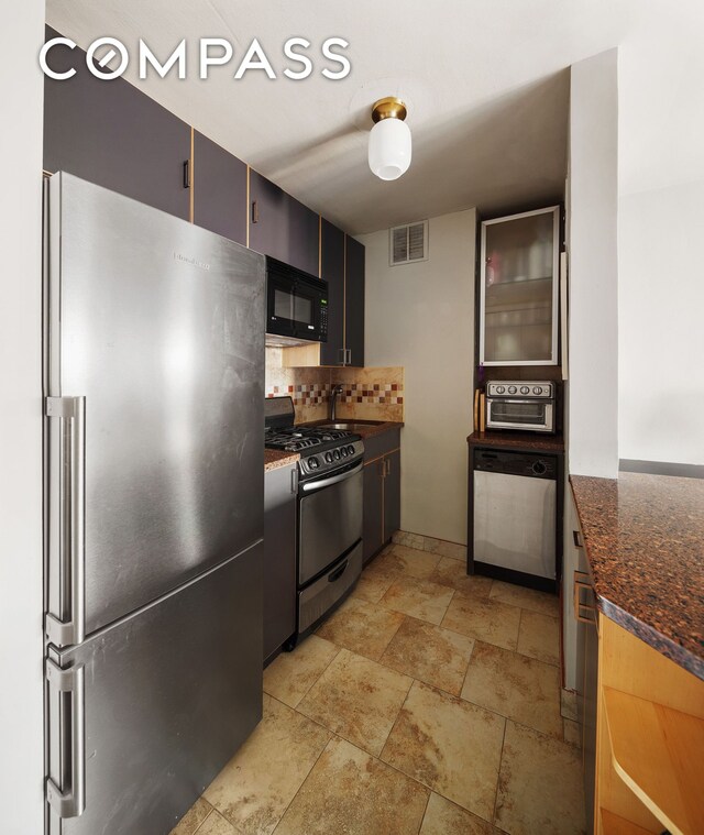 kitchen featuring visible vents, stone finish flooring, backsplash, stainless steel appliances, and dark stone counters