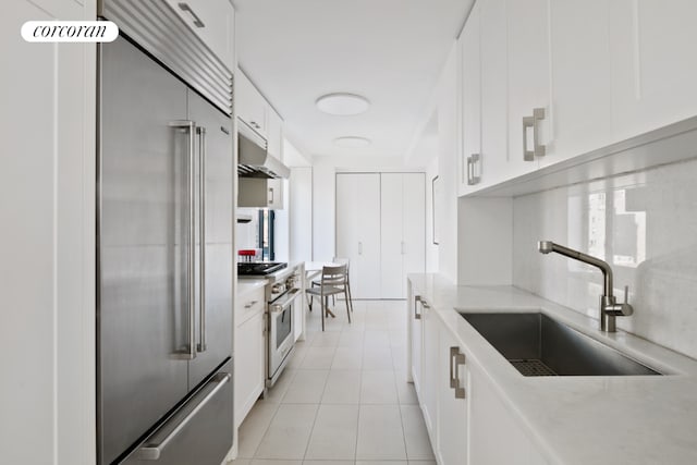 kitchen featuring high end appliances, light countertops, white cabinetry, a sink, and exhaust hood