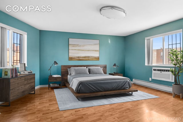 bedroom featuring baseboard heating, a wall mounted air conditioner, light wood-style flooring, and baseboards