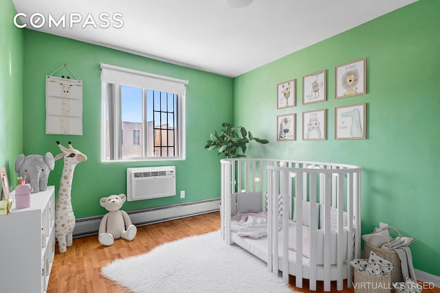 bedroom featuring light wood-style floors, a baseboard radiator, a wall unit AC, and a nursery area