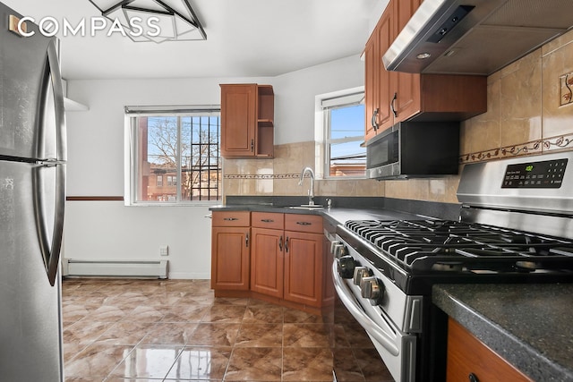 kitchen with brown cabinetry, dark countertops, baseboard heating, stainless steel appliances, and exhaust hood