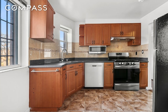 kitchen with tasteful backsplash, dark countertops, appliances with stainless steel finishes, a sink, and under cabinet range hood