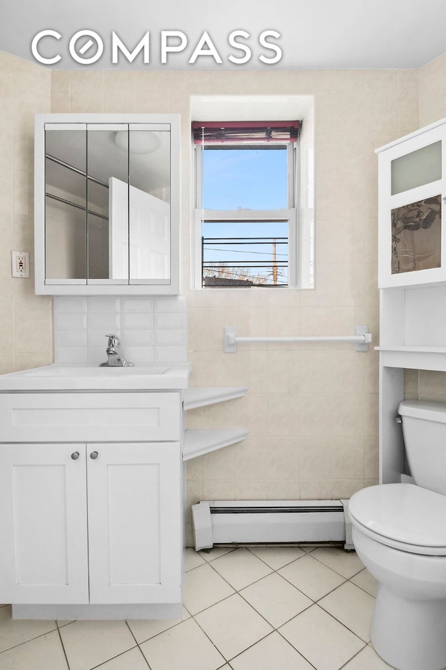 bathroom with a baseboard radiator, toilet, vanity, tile walls, and tile patterned floors