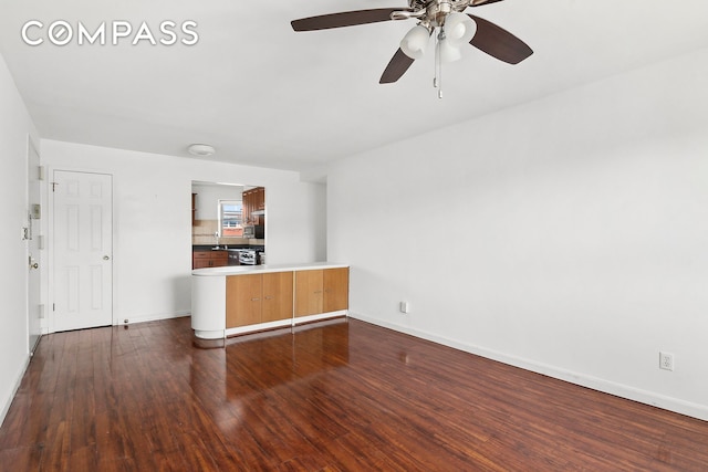 unfurnished living room featuring dark wood-style floors, ceiling fan, and baseboards