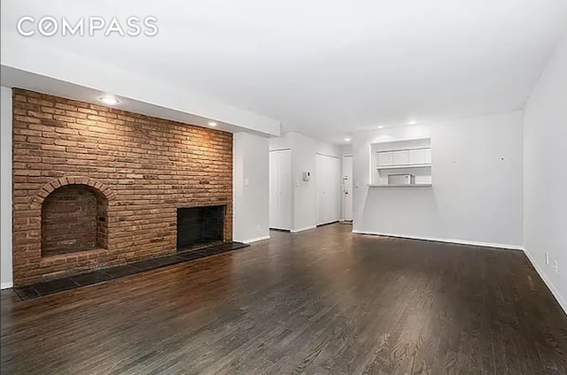 unfurnished living room featuring dark wood-type flooring and a brick fireplace