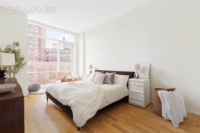 bedroom with expansive windows, light wood finished floors, a view of city, and baseboards