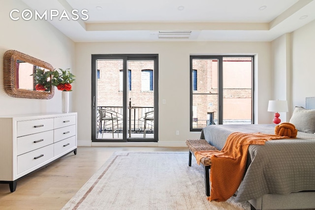 bedroom with a raised ceiling, light hardwood / wood-style floors, and access to outside