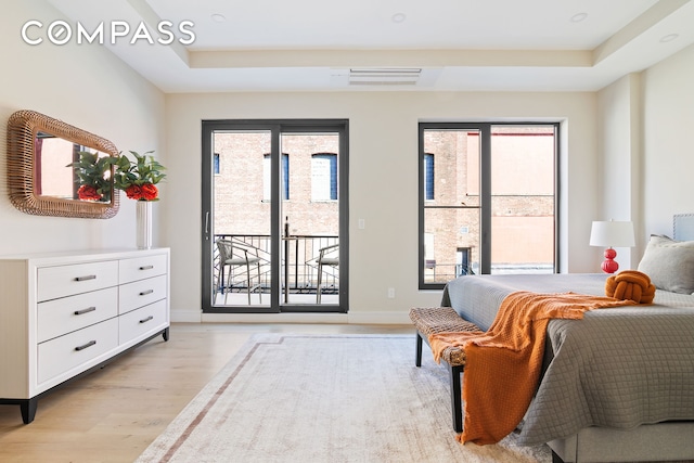 bedroom featuring visible vents, baseboards, a tray ceiling, light wood-style floors, and access to outside